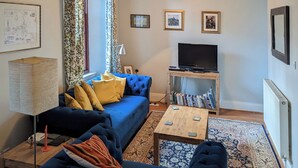 Ein Wohnzimmer mit einem blauen Sofa, einem Couchtisch, einem Fernseher auf einem Holzboden und einem Bücherregal.