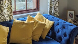 Ein blaues Sofa mit gelben Kissen in einem Zimmer mit Fenster und gemusterten Vorhängen.