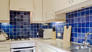 Eine Küche mit weißen Schränken, einem Gasherd, einem Backofen, einer Spüle und einer blau gefliesten Spritzschutzwand.