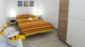 Ein Schlafzimmer mit einem Bett, zwei Nachttischen, einem Beistelltisch, einem Korbwesen mit gelben Blumen und zwei Wandbildern.