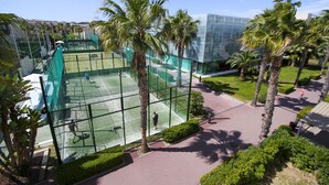 Ein Tennisplatz, umgeben von Palmen und einem Glasgebäude.