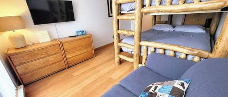 A room with a bunk bed, a flat-screen TV mounted on the wall, a wooden dresser, and a sofa with a patterned pillow.
