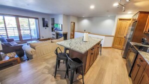 A modern kitchen with a central island, wooden cabinets, and a dining area with a sofa and chairs. - Luxe Downtown Winter Park Condo + Hot Tubs - 3 Full Baths -  Steps to Shuttle (Winter Park)