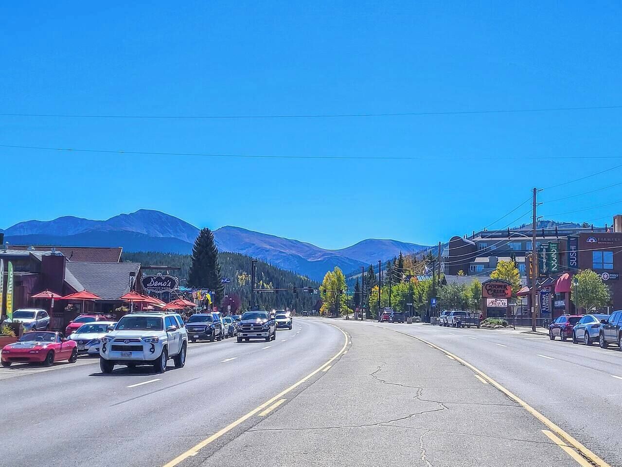 A street view with cars, buildings, and mountains in the background.