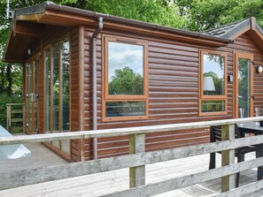 Eine Holzhütte mit großen Fenstern, einer Terrasse und einem kleinen Tisch.
