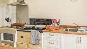 Une cuisine équipée d’une cuisinière, d’un four et d’une horloge murale. On y trouve un panier rempli d’en-cas et une bouteille de vin posée sur le comptoir.
