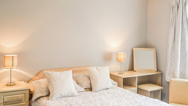 Une chambre à coucher comprenant un lit, des tables de chevet, un bureau, une chaise et un miroir.
