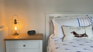 A bedroom with a nightstand, a lamp, a bedside table, and a bed with a pillow featuring a dachshund.