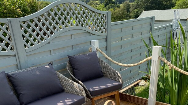 A wooden deck with two wicker sofas and a table, surrounded by a white lattice fence.