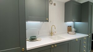 A modern kitchen with grey cabinets, a white countertop, and gold fixtures.