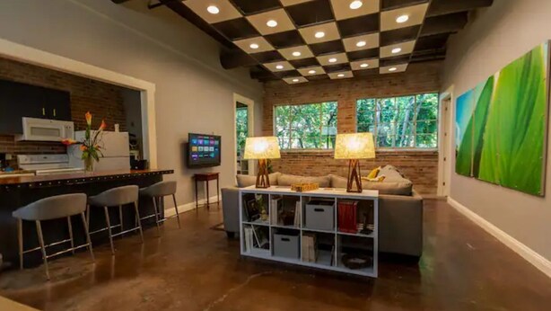 A modern living area with a kitchen, bar stools, a sofa, and a TV. - Incognito #3 : Ground Floor / 1 block from The Scotsman General Store (Laurel)