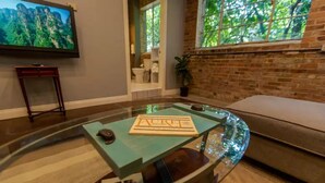 A living room with a glass coffee table displaying a framed certificate, a television mounted on the wall, and a brick wall with a window. - Incognito #3 : Ground Floor / 1 block from The Scotsman General Store (Laurel)