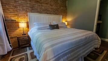 A neatly made bed with a striped bedspread and pillows, a white headboard, and a brick wall behind it.