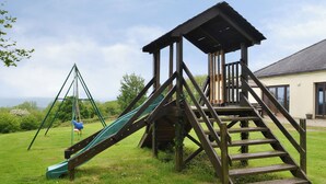 A playground with a slide and swing set, wooden climbing structure, and a house in the background.