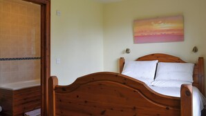 A bedroom with a wooden bed, a painting on the wall, and a bathroom with a shower and tiled walls.