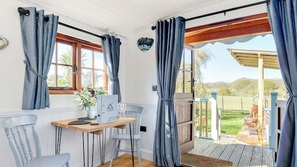 A cozy room with a wooden desk, two chairs, a vase with flowers, and a view of a garden through a sliding door.