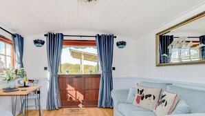 A cozy room with a light blue sofa, a wooden dining table with chairs, a patterned rug, and a wooden gate leading outside.