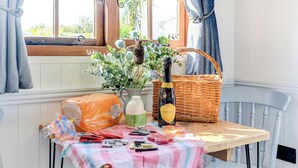 A kitchen table with a wicker basket, a bottle of Prosecco, a loaf of bread, and a variety of food items.