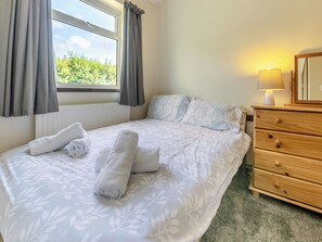 Quarto de hotel com cama, penteadeira, abajur e janela com cortinas.