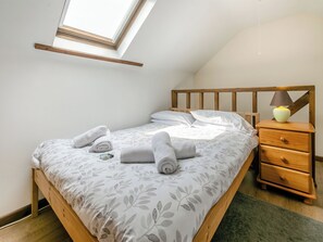 Quarto com teto inclinado, claraboia, estrutura de cama de madeira, mesa de cabeceira com luminária e tapete verde.