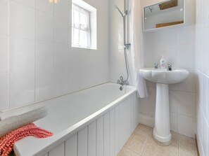 A bathroom with a bathtub, a sink, a window, and a mirror.