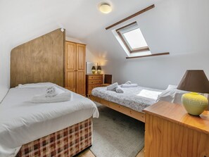 A bedroom with two beds, a wooden wardrobe, a desk with a lamp, and a skylight.