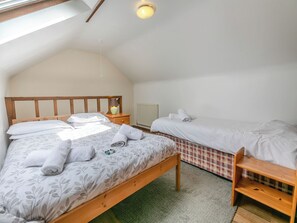 A bedroom with a wooden bed, a nightstand, a lamp, a radiator, and a small wooden bench. - 16 Beech Cottage-UK38936 (Lands End, near Porthcurno)