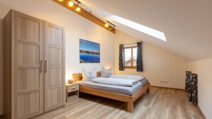 A bedroom with a wooden bed, a nightstand, a wardrobe, a skylight, and a painting of a lake. - Cozy vacation apartment in the Isarwinkel (Gaißach)
