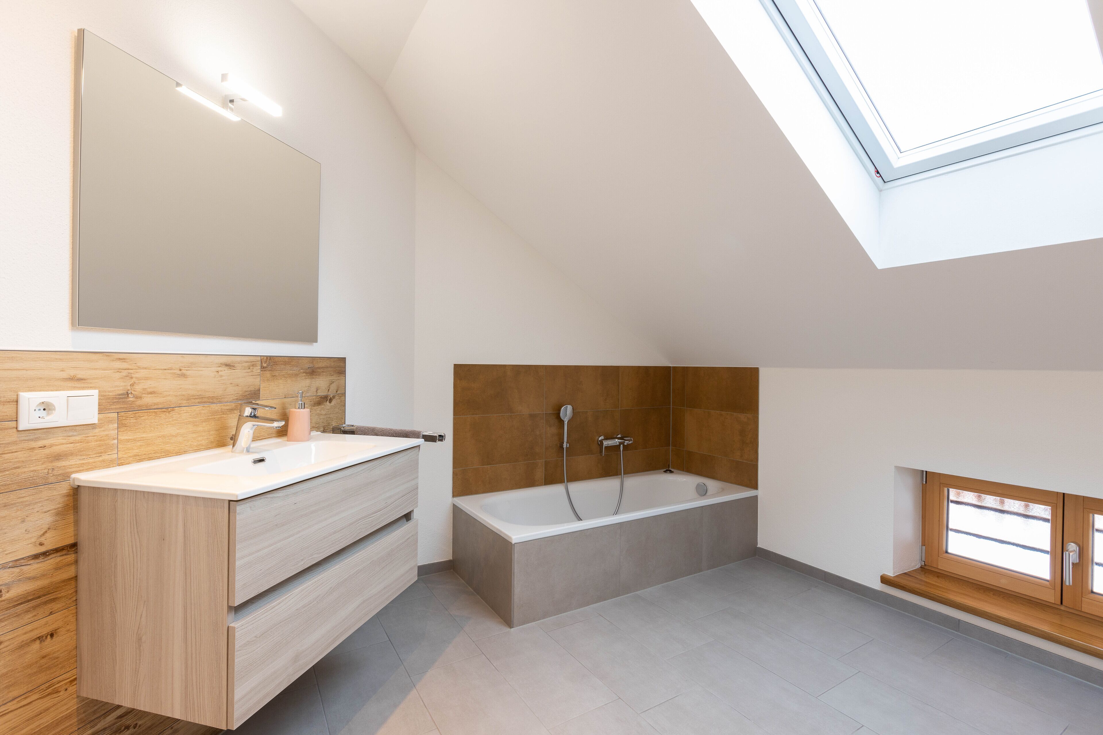 Un baño moderno con tragaluz, una bañera independiente y un tocador de madera.