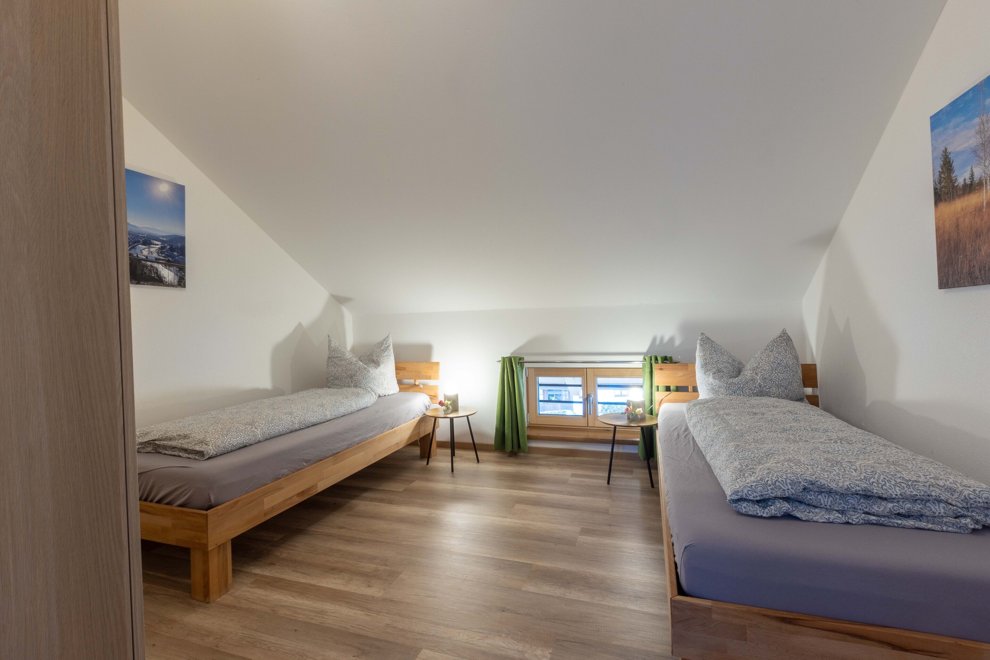 A bedroom with two single beds, a small table, and a window with curtains.