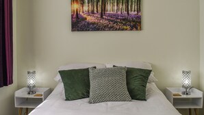 Een slaapkamer met een bed, twee nachtkastjes, een aan de muur bevestigd schilderij van een bos en een raam met gordijnen.