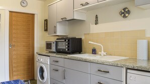 Een kleine keuken met een magnetron, broodrooster, spoelbak en wasmachine.