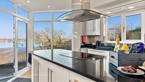 Eine moderne Küche mit einer großen Kochinsel, Edelstahlgeräten und großen Fenstern mit Blick ins Freie.