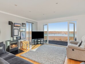 Una sala de estar moderna con chimenea, televisor de pantalla plana, sofá, sillón reclinable y un ventanal con vista a un lago.