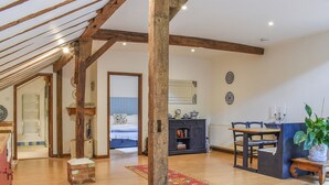 A spacious room with wooden beams, a dining area with a table and chairs, a fireplace, and a bed with a blue headboard. - 1 bedroom accommodation in Hadlow Down (Hadlow Down)