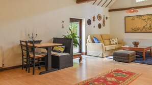 A spacious living area with a dining table, chairs, a sofa, and a coffee table. There is a large window providing natural light and a view of greenery outside. - 1 bedroom accommodation in Hadlow Down (Hadlow Down)