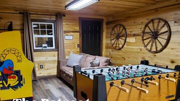 A cozy room with a foosball table, a sofa, and a wooden wall with a sign that says "enjoy".