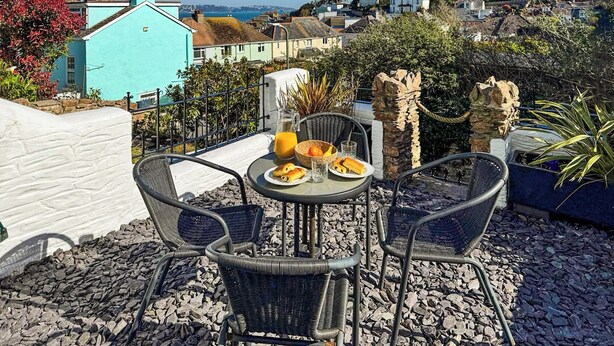 A terrace with a table set for breakfast, overlooking a coastal town. - 2 bedroom accommodation in Brixham (Brixham)