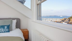A bedroom with a bed, a nightstand, a radiator, and a window with a view of a marina and boats. - 2 bedroom accommodation in Brixham (Brixham)