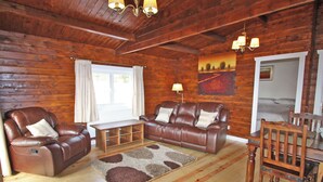 A cozy log cabin interior with a leather sofa, armchairs, a wooden dining table, and a chandelier. - White Springs - Lake view (Pontardulais, Swansea)
