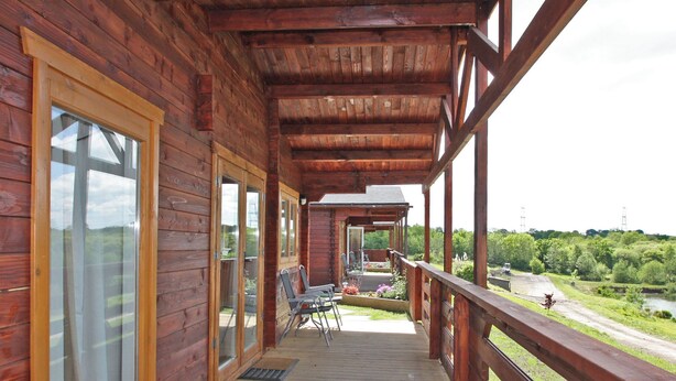 A wooden cabin with a covered porch, large windows, and a view of a river and greenery. - White Springs - Lake view (Pontardulais, Swansea)