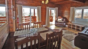 A wooden cabin interior with a dining table, chairs, a leather sofa, and a fireplace. - White Springs - Lake view (Pontardulais, Swansea)