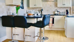 A modern kitchen with white cabinets, a stainless steel range hood, and two black bar stools.