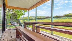 A wooden deck with a hanging chair and a bench, overlooking a green field.