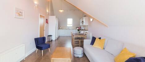A spacious living area with a high ceiling, a dining table, and a sofa with cushions.