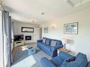 Una sala de estar con un sofá azul, un televisor, una chimenea y una puerta que da a otra habitación.