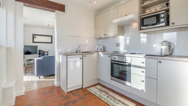Une cuisine moderne avec des meubles blancs, un four à micro-ondes encastré, un lave-vaisselle et un revêtement mural en carreaux.