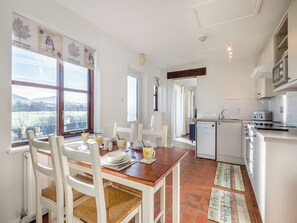 Una cocina moderna con electrodomésticos blancos, un comedor con mesa de madera y sillas blancas, y grandes ventanas que ofrecen vistas al exterior.