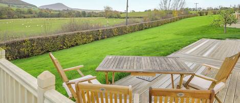 Una terraza con muebles de madera da a un campo de hierba con ovejas.
