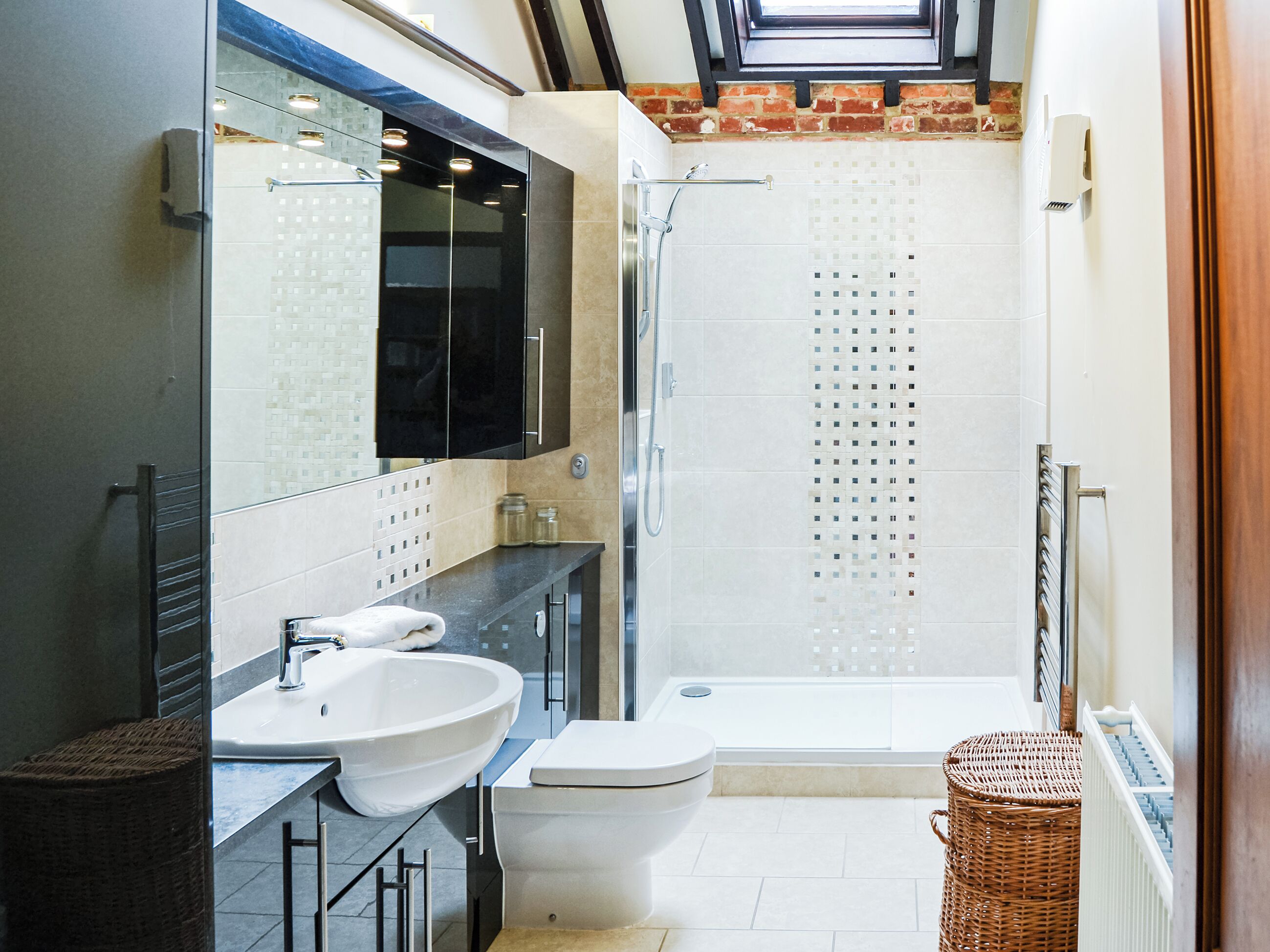 A modern bathroom with a skylight, a walk-in shower, and a large mirror.